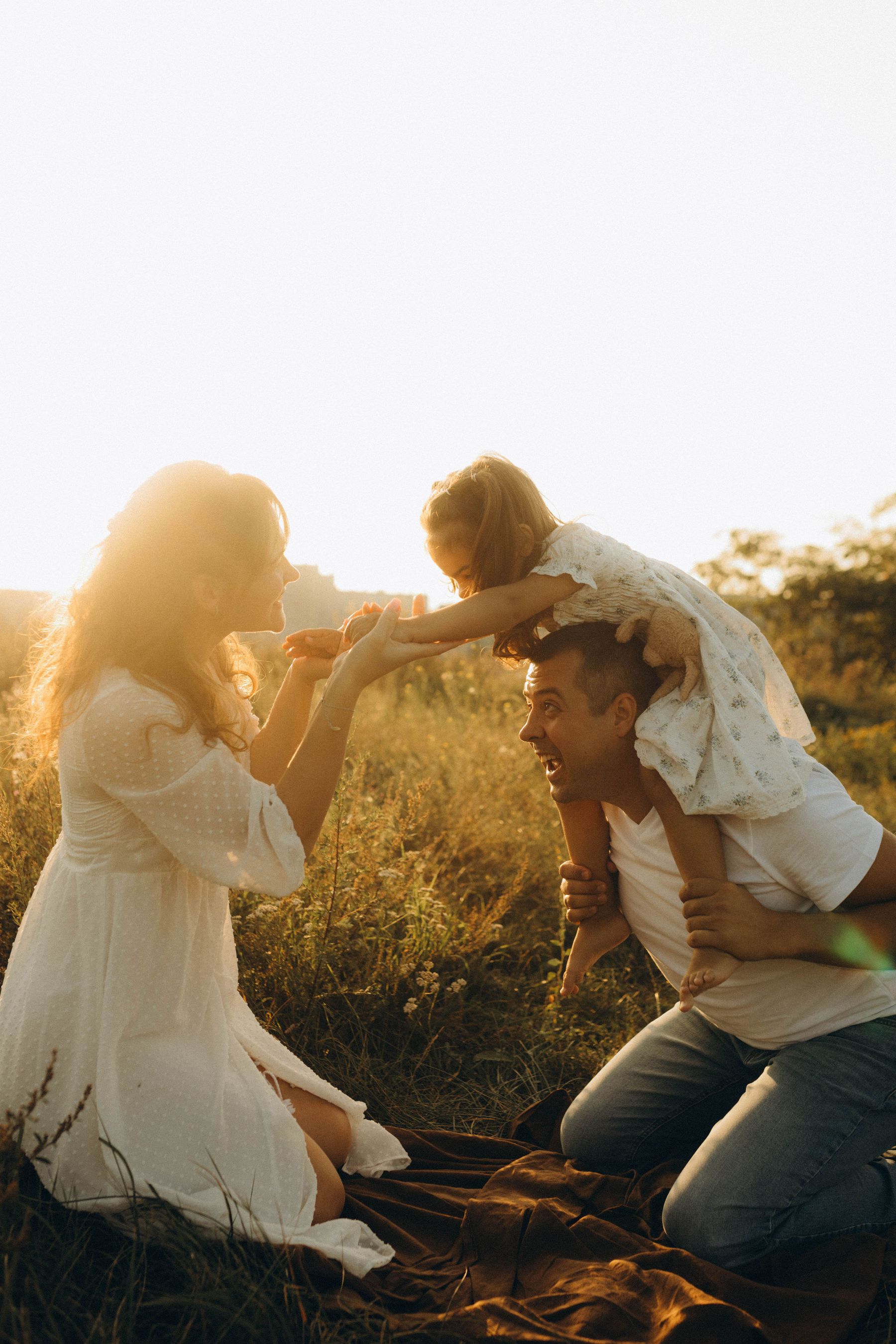 Placeholder: Parents playing with their child in a sunny field
